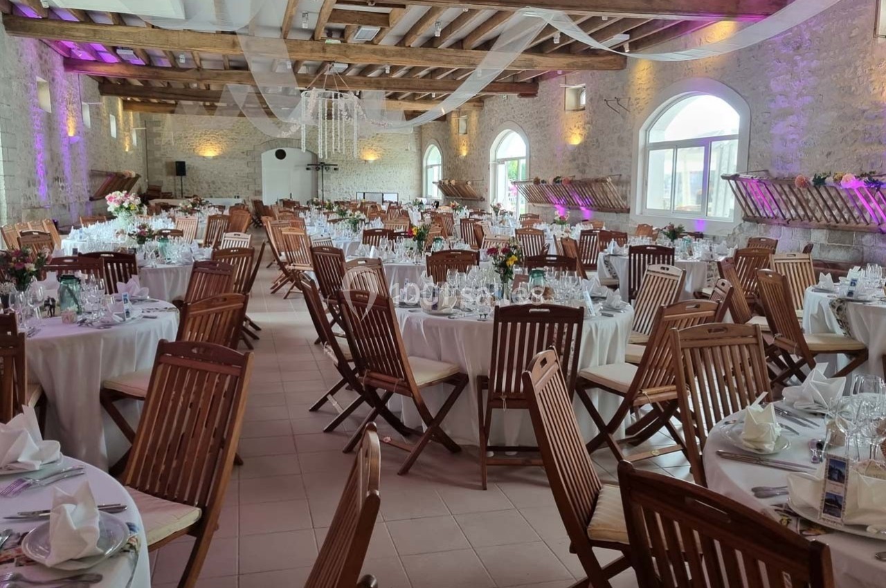 Salle de réception lumineuse avec tables rondes dressées, chaises en bois et décorations élégantes.