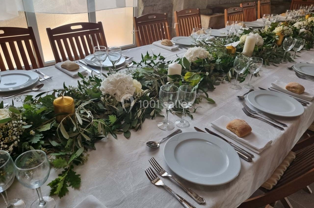 Table dressée avec une nappe blanche, vaisselle, couverts, bougies et décoration florale verte et blanche.
