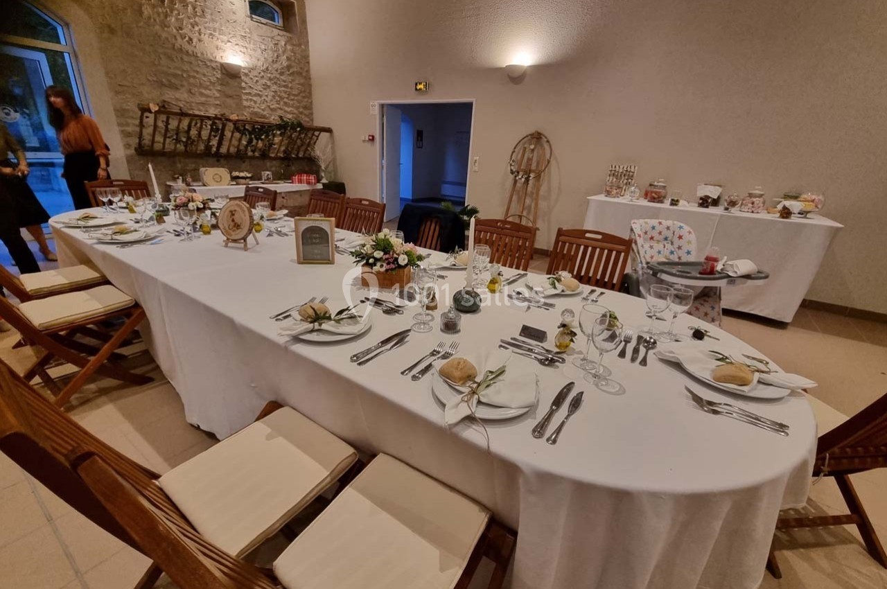 Table dressée pour un repas dans une salle avec murs en pierre, décorations florales et vaisselle disposée.