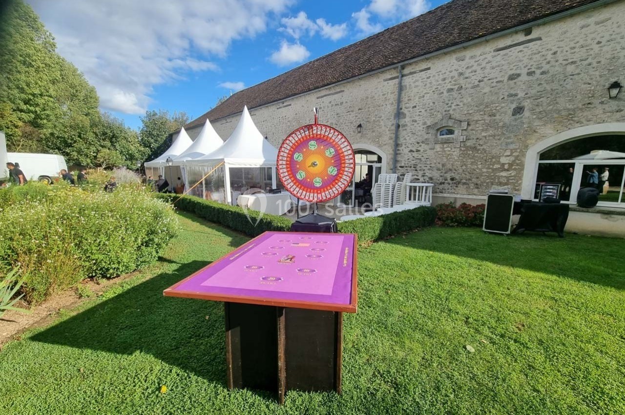 Table de jeu et roue colorée installées sur une pelouse devant un bâtiment en pierre et des tentes blanches.