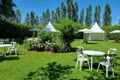 Chaises blanches disposées en rangées sur une pelouse, face à une petite scène décorée pour un événement en plein air.