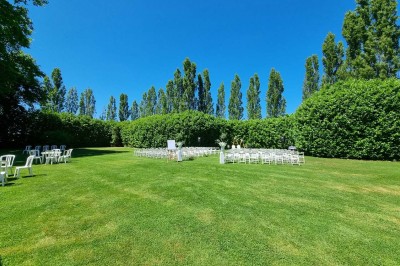 Chaises blanches disposées en rangées sur une pelouse, face à une petite scène décorée pour un événement en plein air.