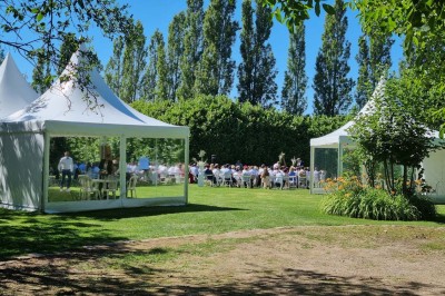 Chaises blanches disposées en rangées sur une pelouse, face à une petite scène décorée pour un événement en plein air.