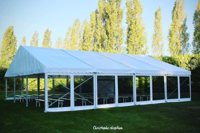 Chaises blanches disposées en rangées sur une pelouse, face à une petite scène décorée pour un événement en plein air.