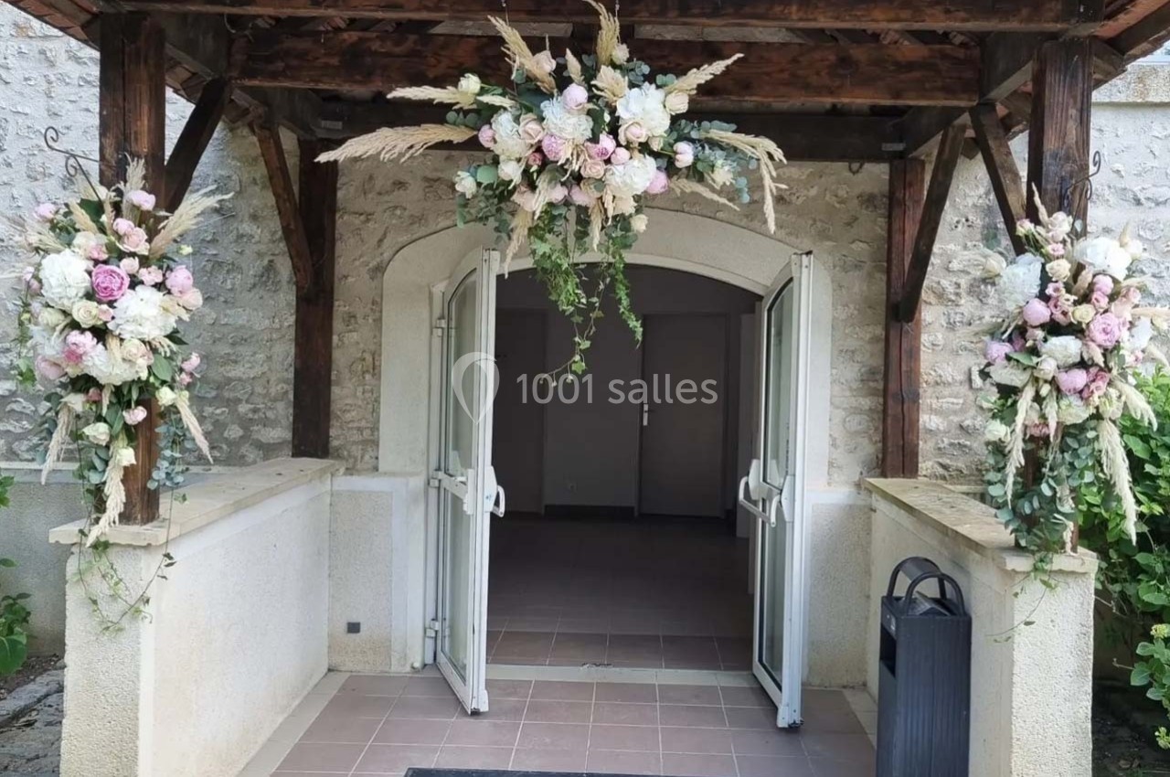 Entrée en pierre avec portes ouvertes, décorée de compositions florales pastel suspendues et sur les côtés.