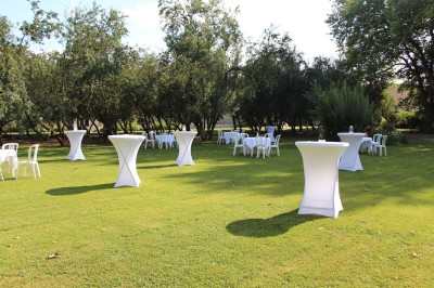 Chaises blanches disposées en rangées sur une pelouse, face à une petite scène décorée pour un événement en plein air.
