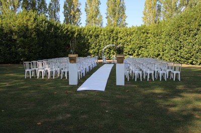 Chaises blanches disposées en rangées sur une pelouse, face à une petite scène décorée pour un événement en plein air.
