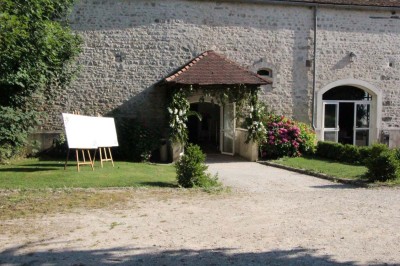 Chaises blanches disposées en rangées sur une pelouse, face à une petite scène décorée pour un événement en plein air.