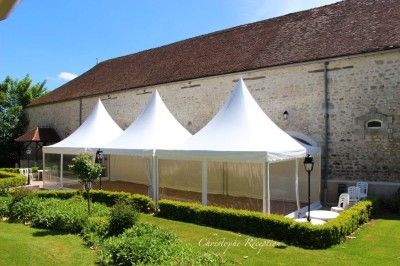 Chaises blanches disposées en rangées sur une pelouse, face à une petite scène décorée pour un événement en plein air.