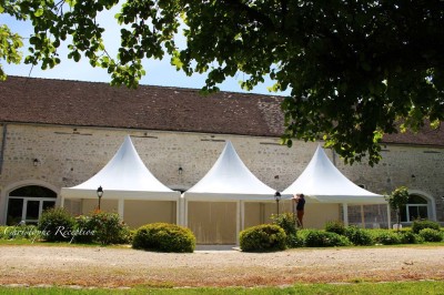 Chaises blanches disposées en rangées sur une pelouse, face à une petite scène décorée pour un événement en plein air.