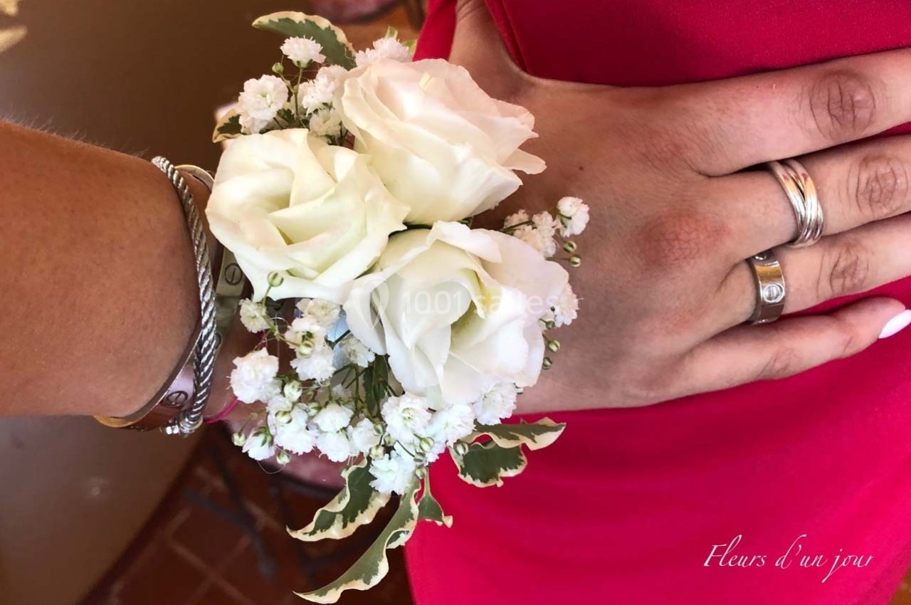 Bracelet floral avec des roses blanches et du gypsophile porté sur un poignet orné de bijoux.