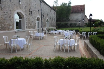 Chaises blanches disposées en rangées sur une pelouse, face à une petite scène décorée pour un événement en plein air.