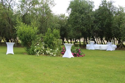 Chaises blanches disposées en rangées sur une pelouse, face à une petite scène décorée pour un événement en plein air.