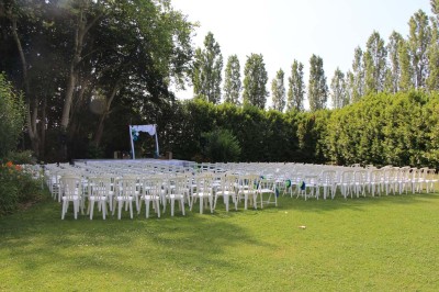 Chaises blanches disposées en rangées sur une pelouse, face à une petite scène décorée pour un événement en plein air.