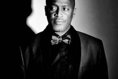 Portrait en noir et blanc d'un homme en costume avec un nœud papillon, éclairé par une lumière latérale.