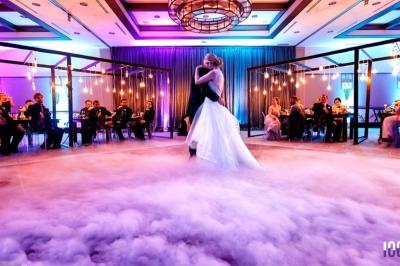 Un couple danse au centre d'une salle de réception éclairée, entouré de fumée et d'invités assis.