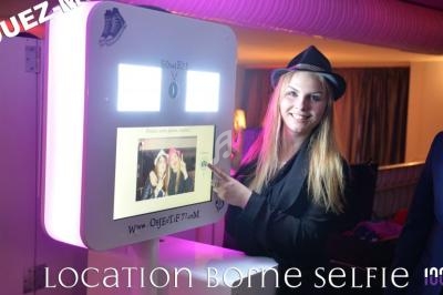 Femme souriante utilisant une borne photo interactive dans un environnement festif, éclairé par des lumières colorées.