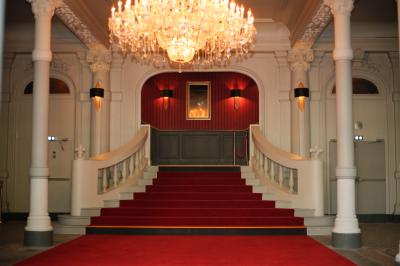 Branches d'arbre avec des feuilles vertes devant une façade en pierre ornée de grandes fenêtres.