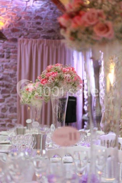 Salle de réception décorée avec des tables dressées et des centres de table composés de fleurs roses et blanches.