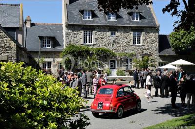 Terrasse en bois avec des chaises noires, adossée à une maison en bardage bois, sous un ciel nuageux.