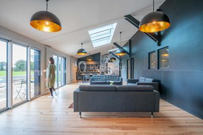 Terrasse en bois avec des chaises noires, adossée à une maison en bardage bois, sous un ciel nuageux.