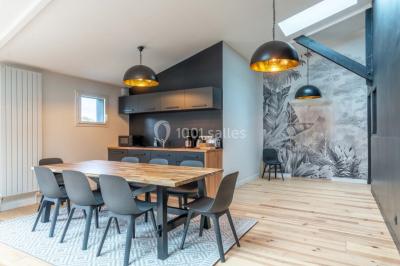 Terrasse en bois avec des chaises noires, adossée à une maison en bardage bois, sous un ciel nuageux.