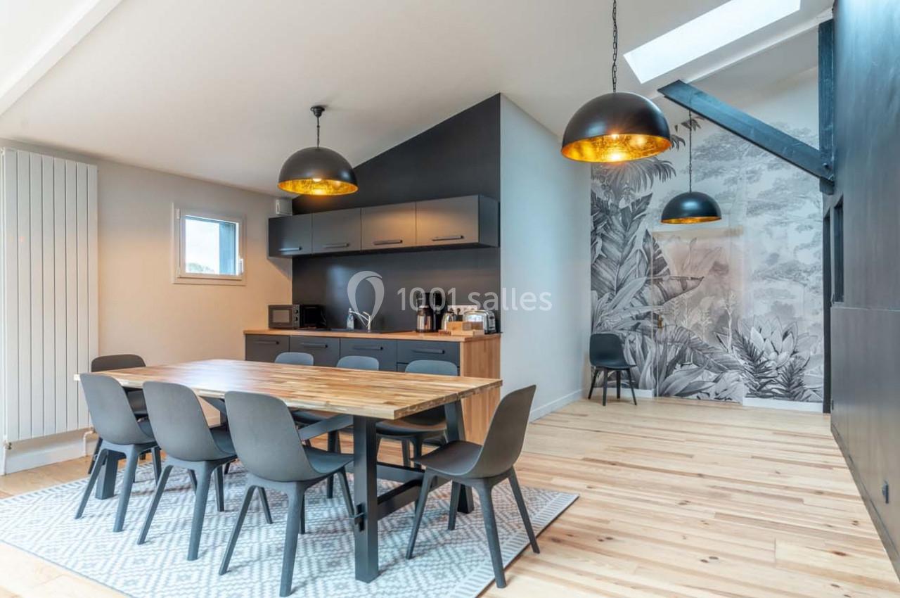 Salle à manger moderne avec table en bois, chaises noires, cuisine ouverte et mur décoré d'une fresque végétale.