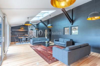 Terrasse en bois avec des chaises noires, adossée à une maison en bardage bois, sous un ciel nuageux.