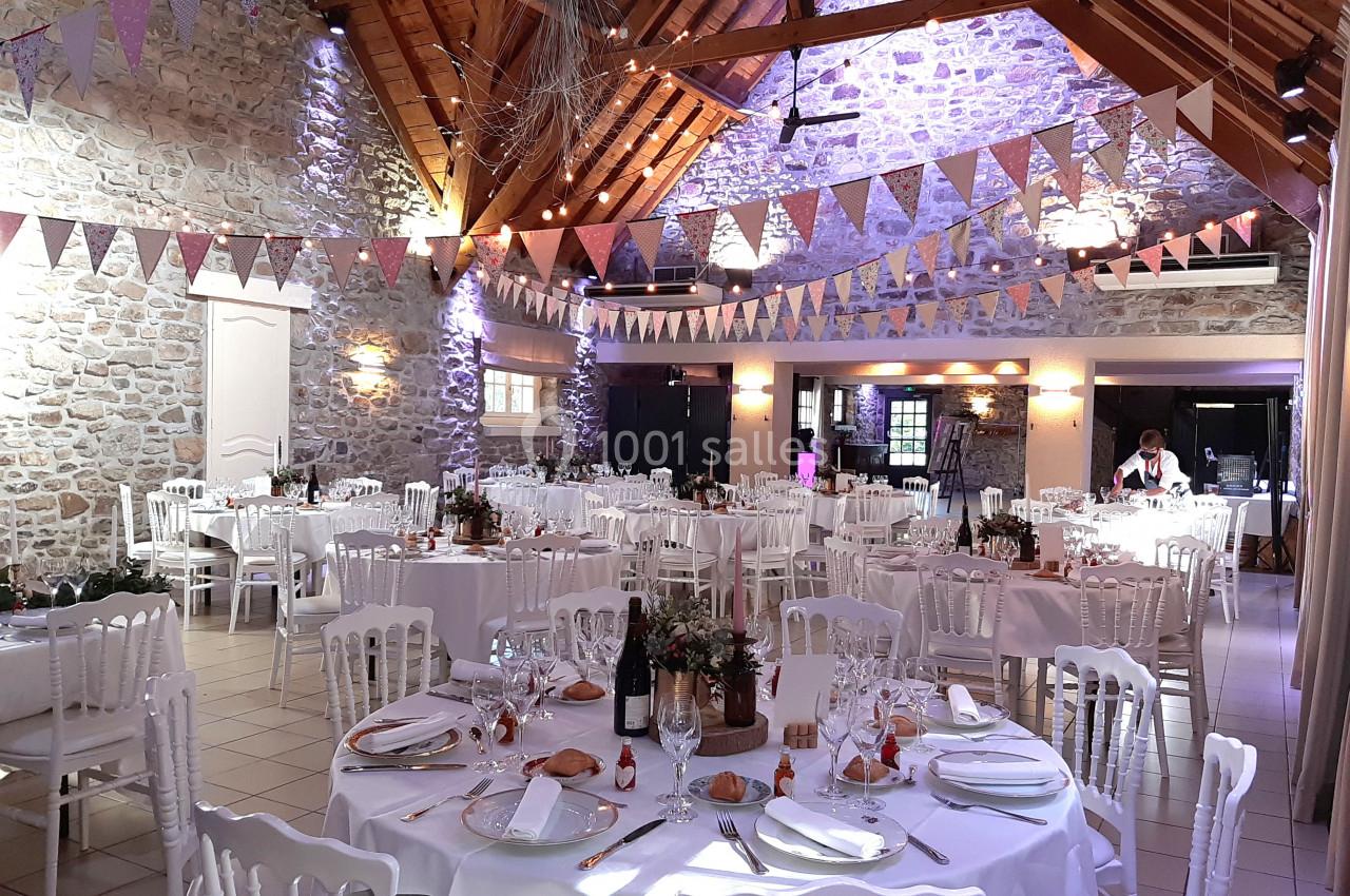 Salle de réception décorée avec des guirlandes et des tables dressées pour un événement festif.