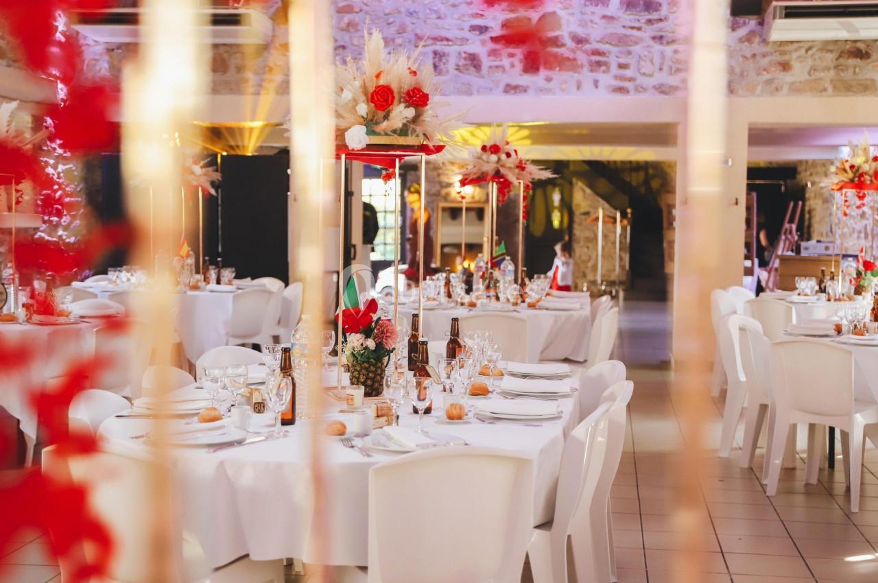 Salle de réception décorée avec des tables rondes, nappes blanches, centres de table floraux et éclairage chaleureux.