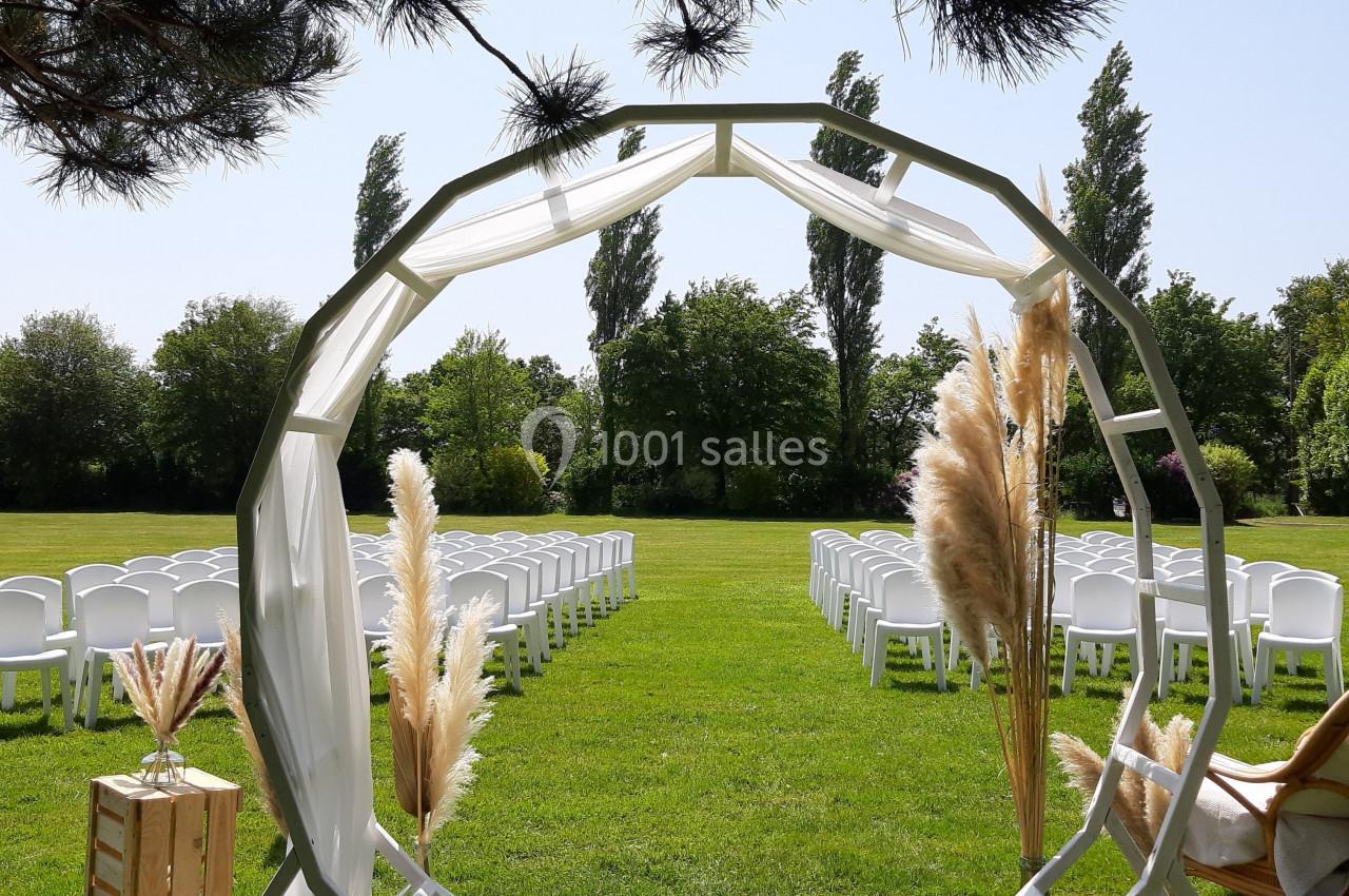 Arche circulaire décorée de pampas sur une pelouse, entourée de chaises blanches disposées pour une cérémonie en plein air.