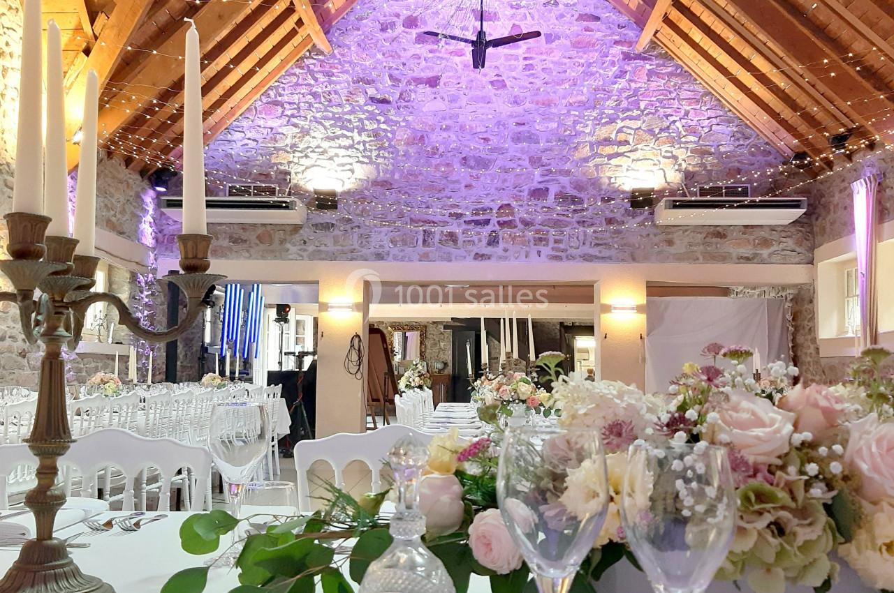 Salle de réception avec poutres apparentes, décor floral sur table dressée et éclairage tamisé.