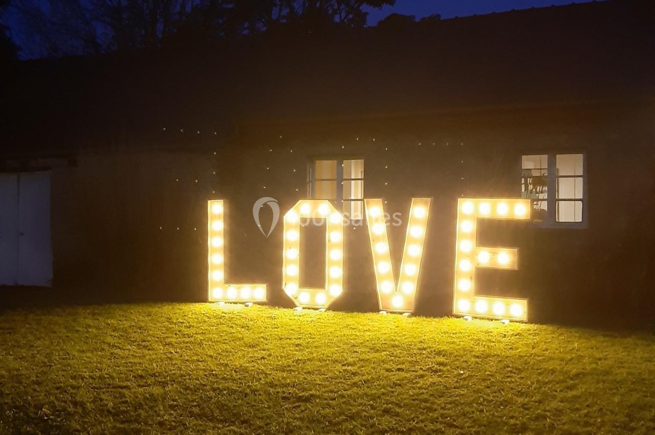 Lettres lumineuses formant le mot ’LOVE’ posées sur une pelouse devant un bâtiment sombre au crépuscule.