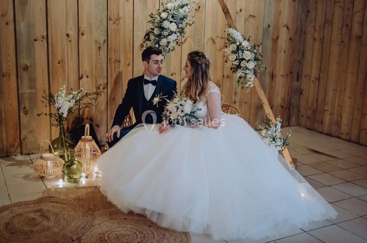 Un couple en tenue de mariage est assis devant une décoration florale dans un cadre en bois chaleureux.