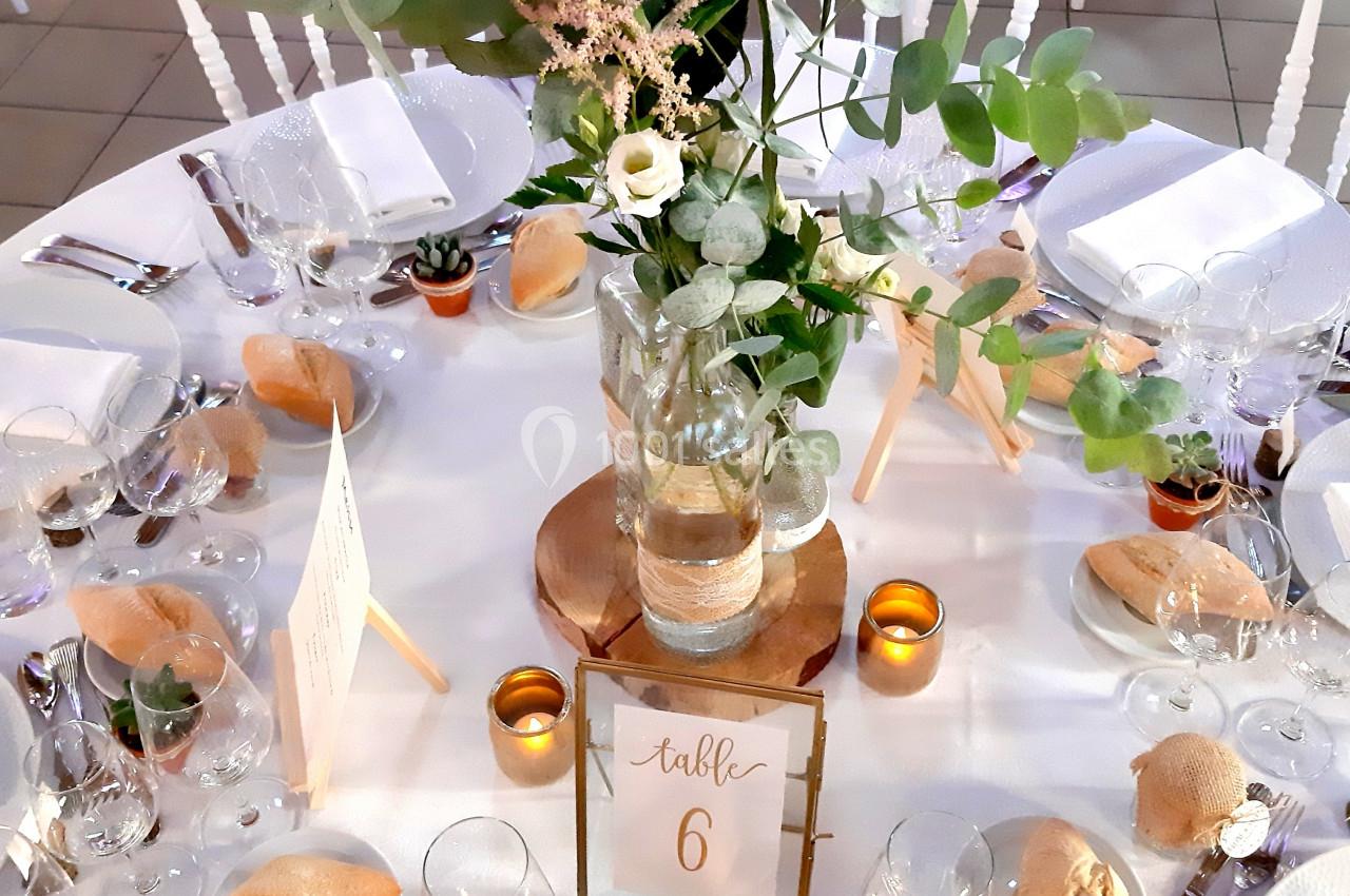 Table de réception décorée avec un centre de table floral, bougies, vaisselle élégante et petits pains disposés.