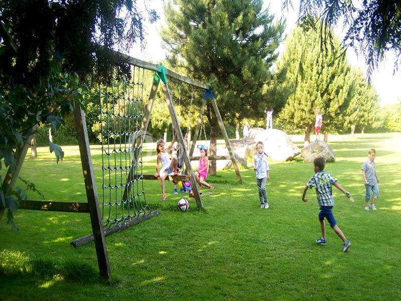 Des enfants jouent près d'une structure de jeux en bois dans un parc verdoyant par une journée ensoleillée.