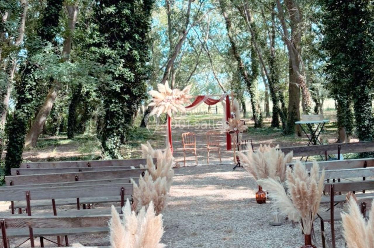 Allée en plein air bordée de bancs en bois, décorée de pampas, menant à une arche rouge dans une forêt verdoyante.