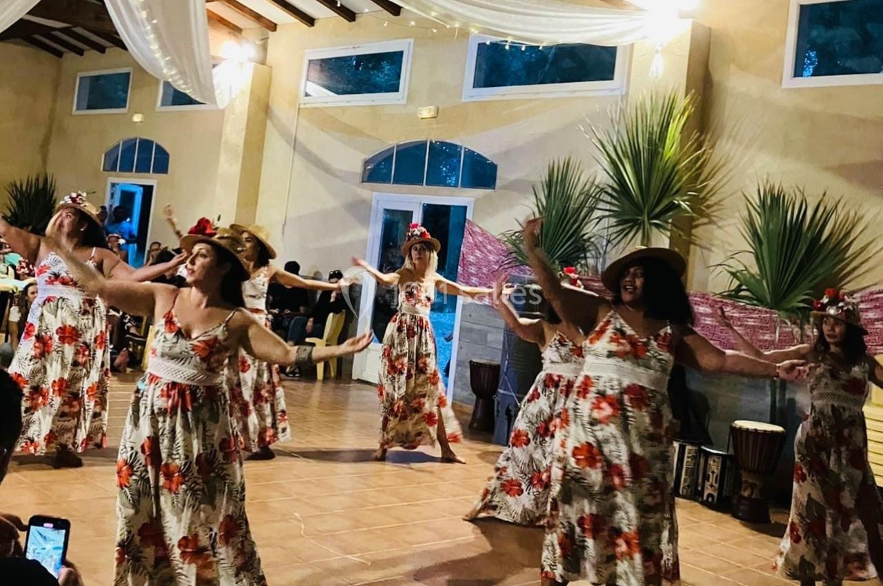 Des femmes en robes fleuries dansent en groupe dans une salle décorée, sous des lumières tamisées.