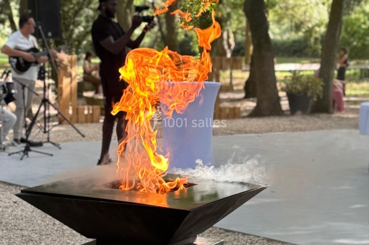 Brasero allumé avec des flammes vives dans un parc arboré, un musicien en arrière-plan.