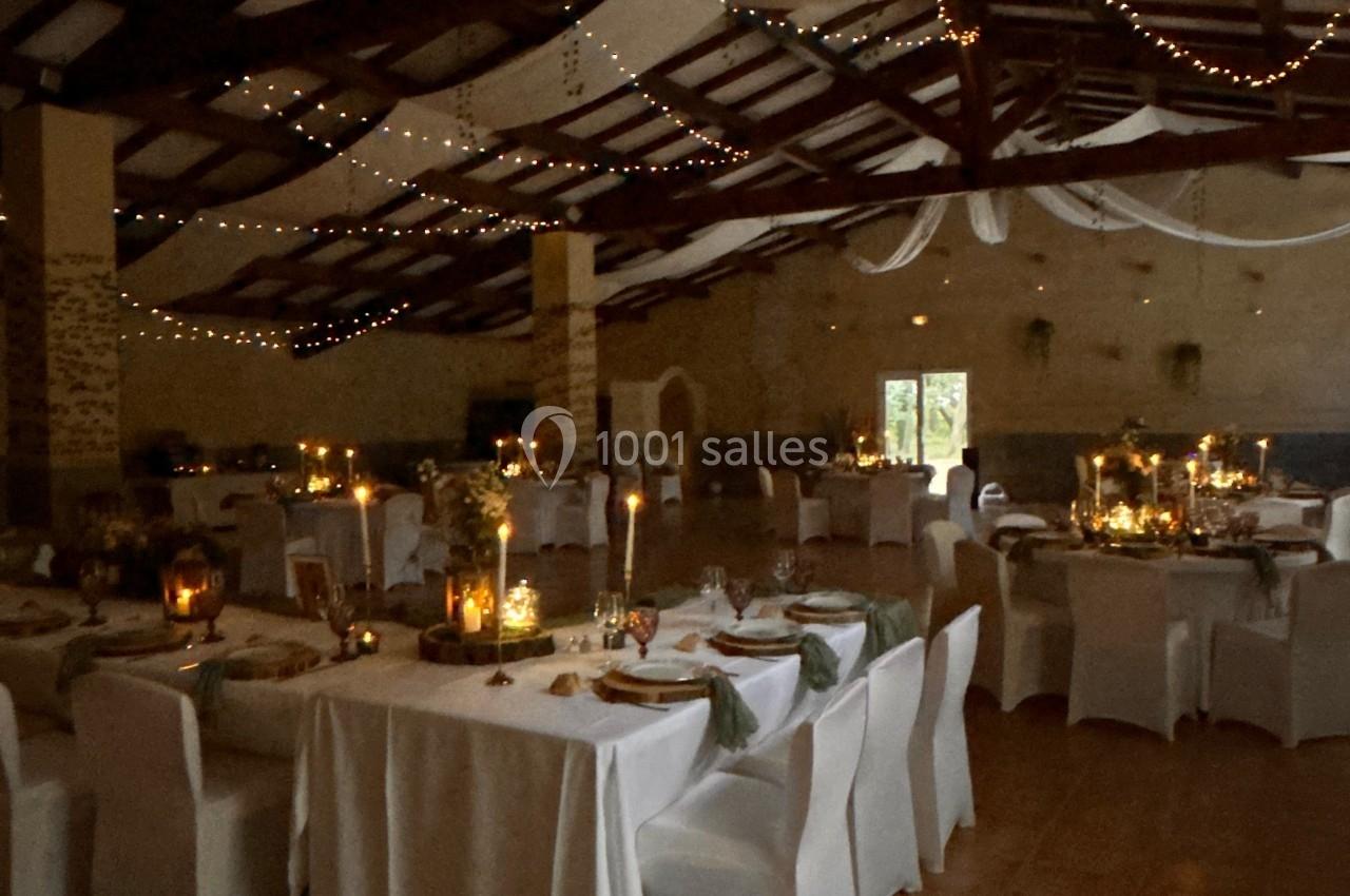 Salle de réception décorée avec des guirlandes lumineuses, des tables dressées et des chaises recouvertes de housses…