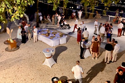 Groupe de personnes réunies en soirée en plein air, avec tables décorées et guirlandes lumineuses suspendues.