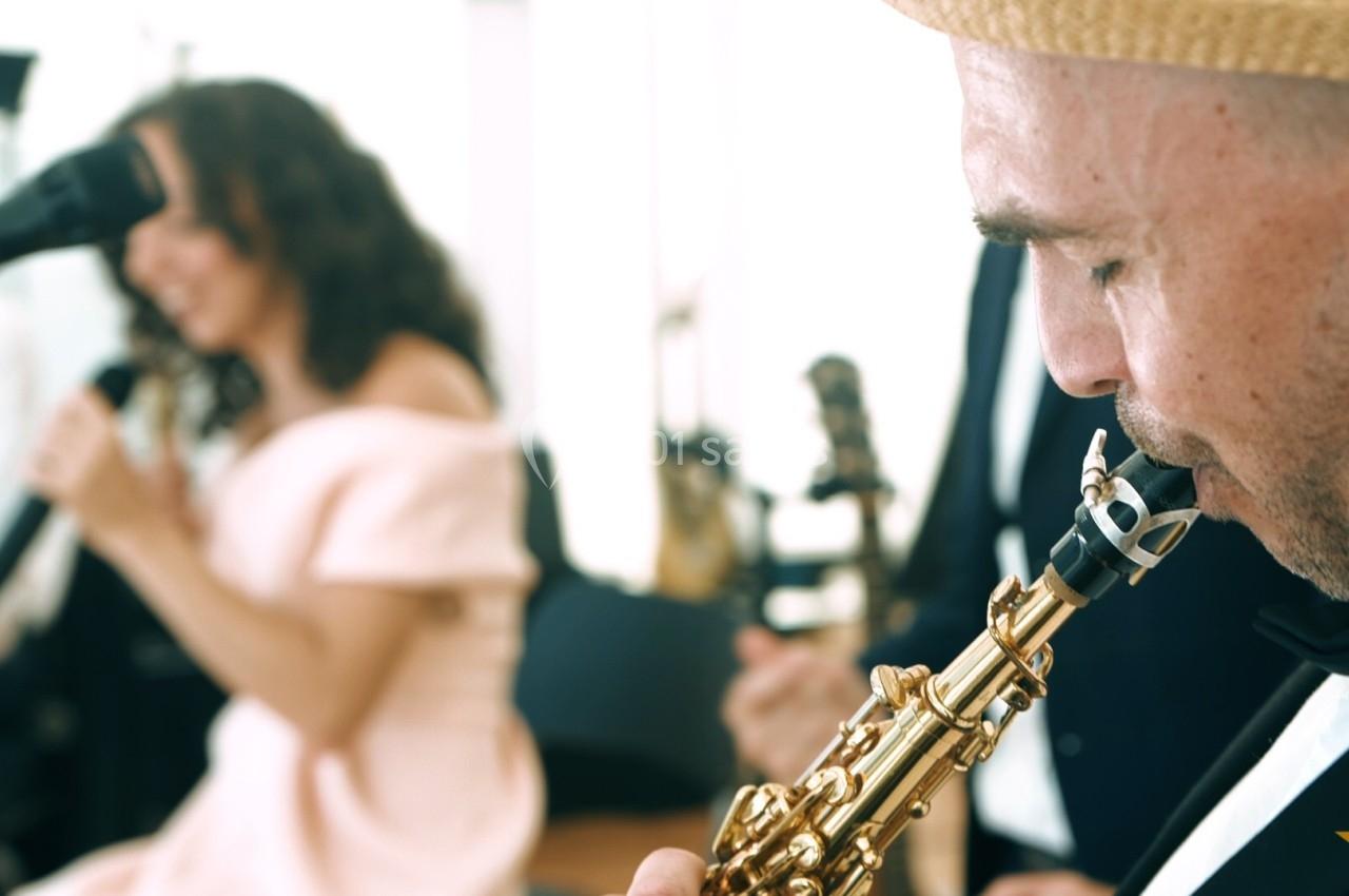 Un musicien joue du saxophone au premier plan tandis qu'une chanteuse se produit en arrière-plan flou.