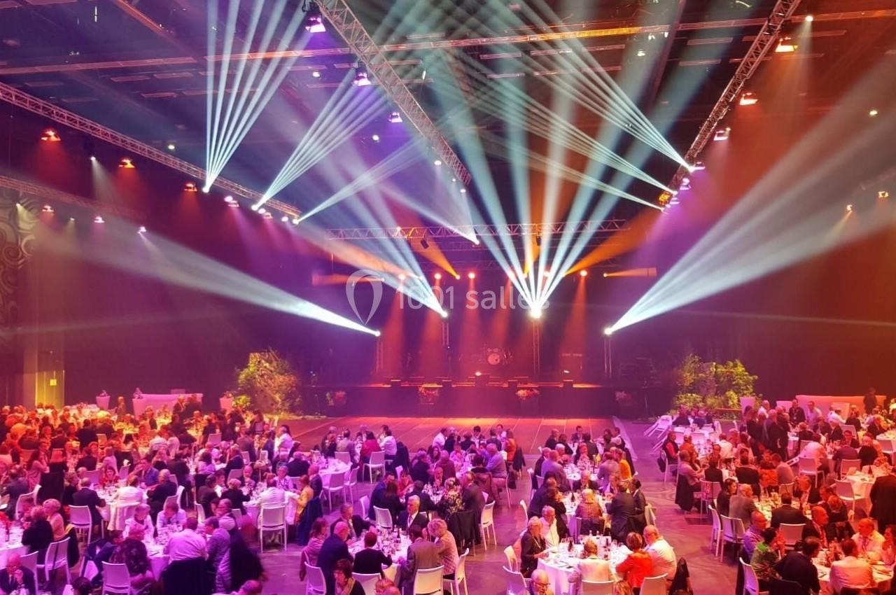 Salle de réception illuminée avec des projecteurs colorés, des tables rondes occupées par des convives.