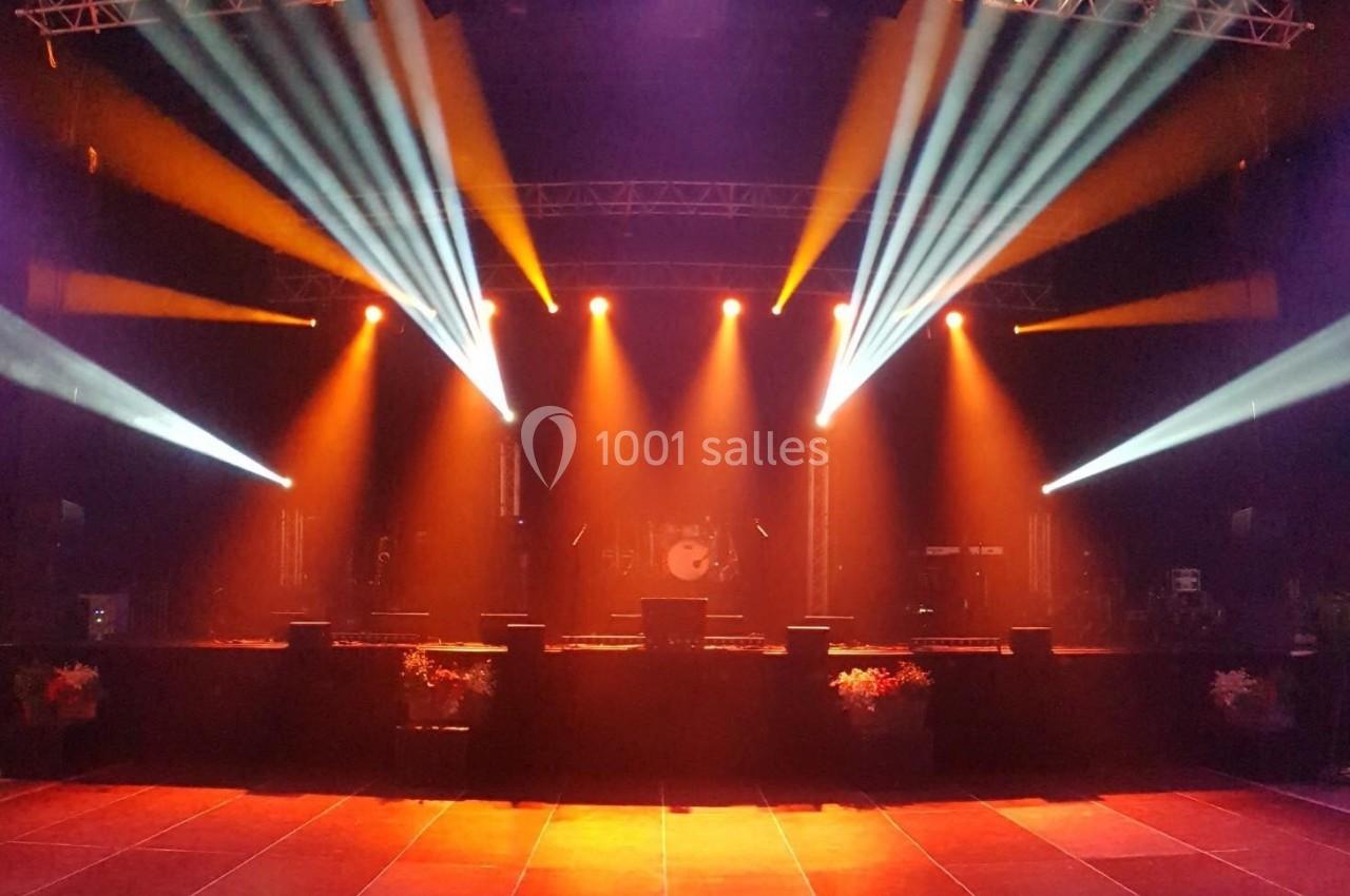 Scène de concert vide illuminée par des projecteurs colorés orange et blancs, avec une batterie en arrière-plan.