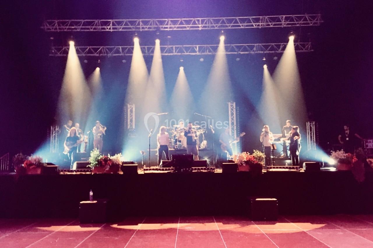 Groupe de musiciens sur une scène éclairée par des projecteurs, avec des fleurs disposées au bord de la scène.