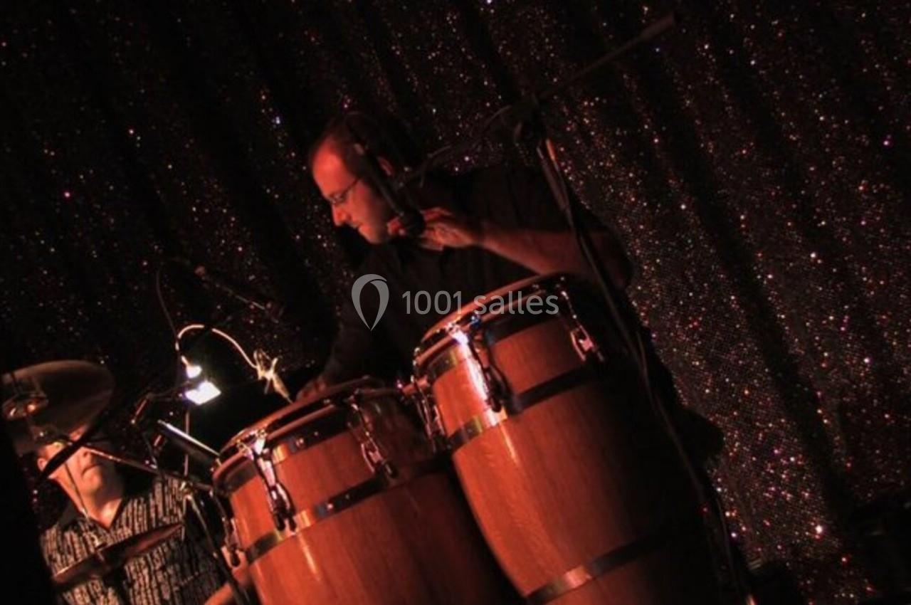 Un musicien joue des congas sur une scène éclairée, avec un fond scintillant sombre.