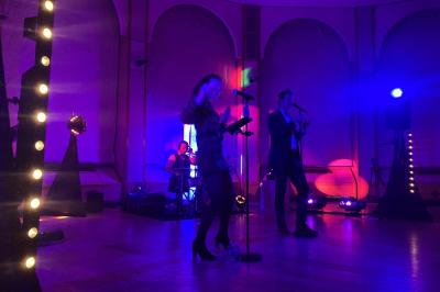 Un groupe de musiciens et une chanteuse se produisent sur scène sous des lumières colorées.