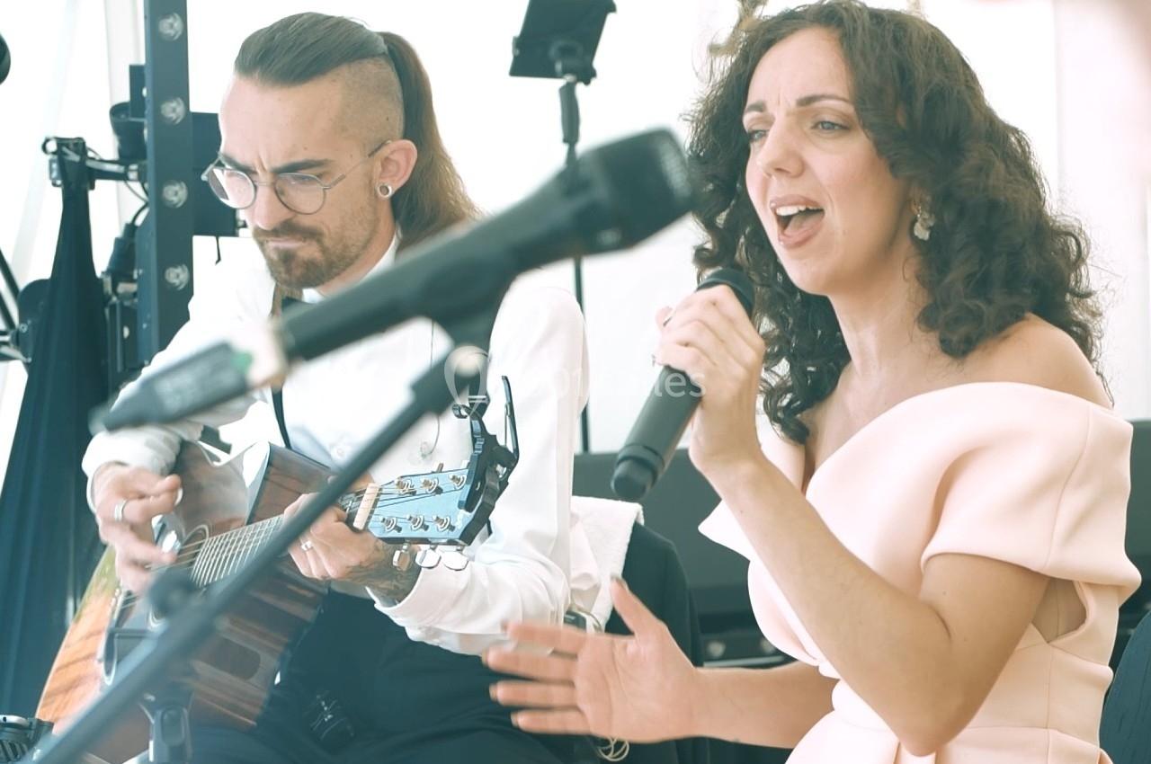 Une chanteuse en robe rose et un guitariste jouent de la musique en direct dans un cadre lumineux.