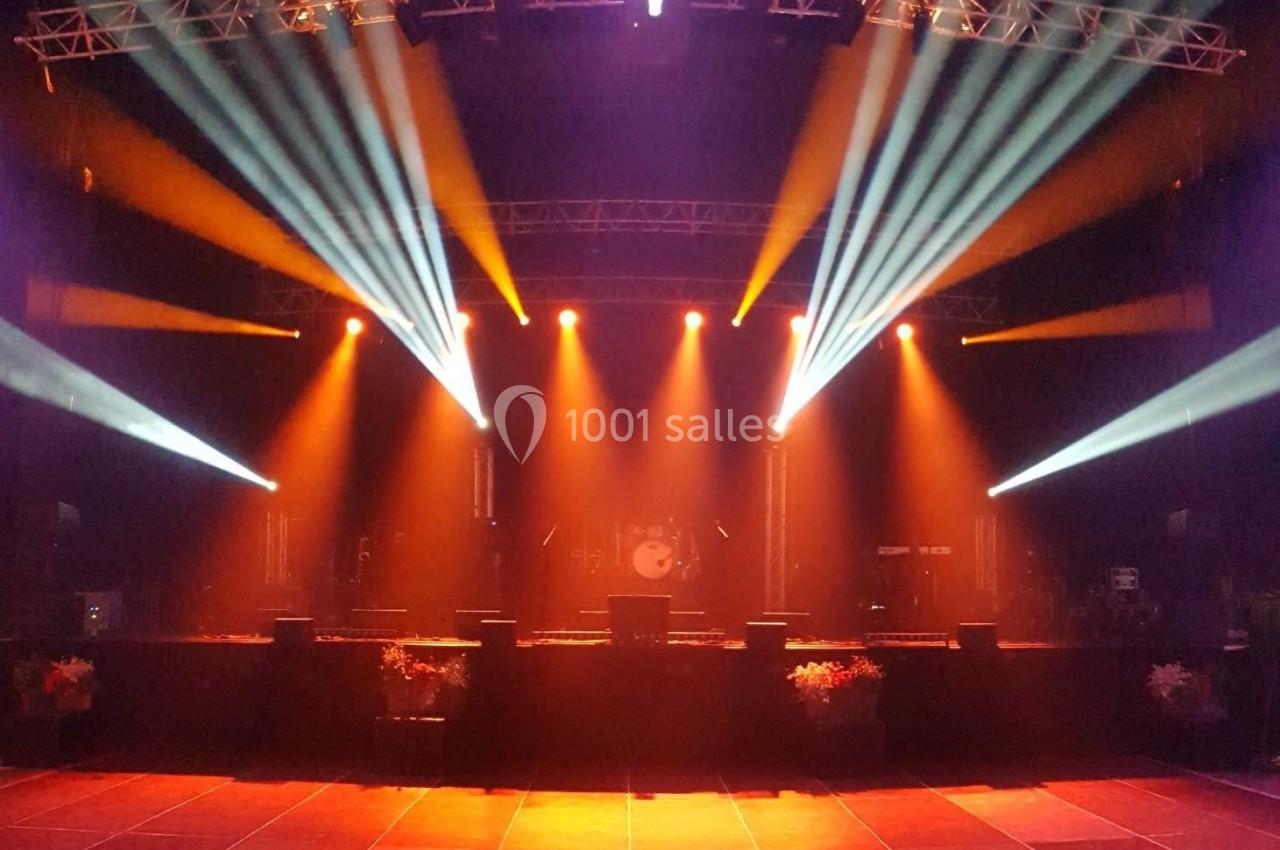 Projecteurs colorés éclairant une scène vide avec des instruments de musique en arrière-plan.