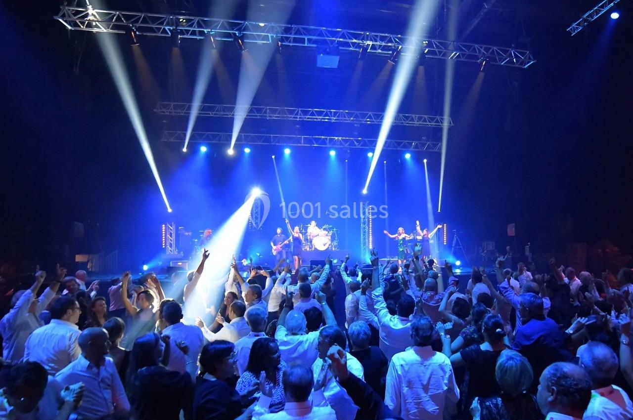 Foule dansant devant un groupe de musiciens sur une scène illuminée par des projecteurs bleus.
